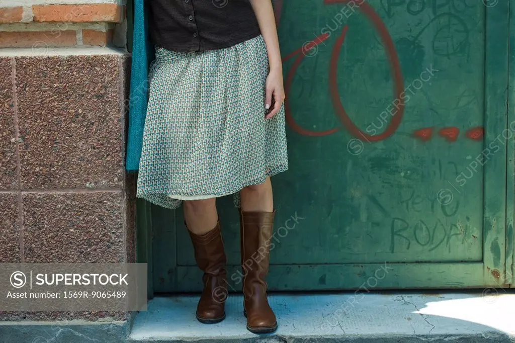 Young woman in trendy clothing leaning against wall, low section