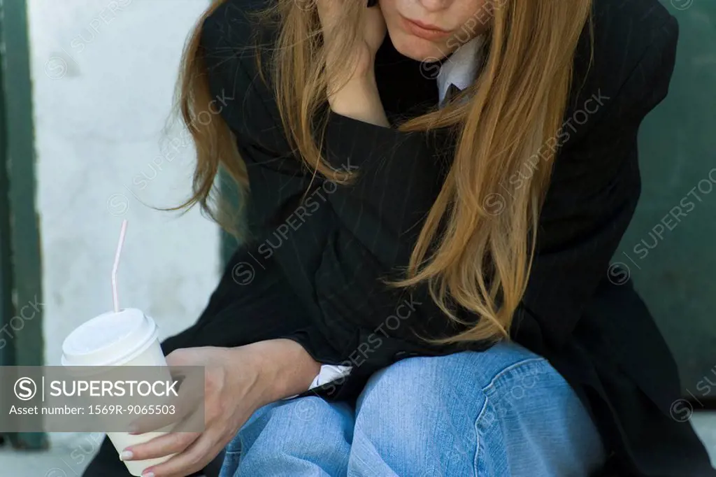 Young woman leaning on elbow, holding cup, cropped view