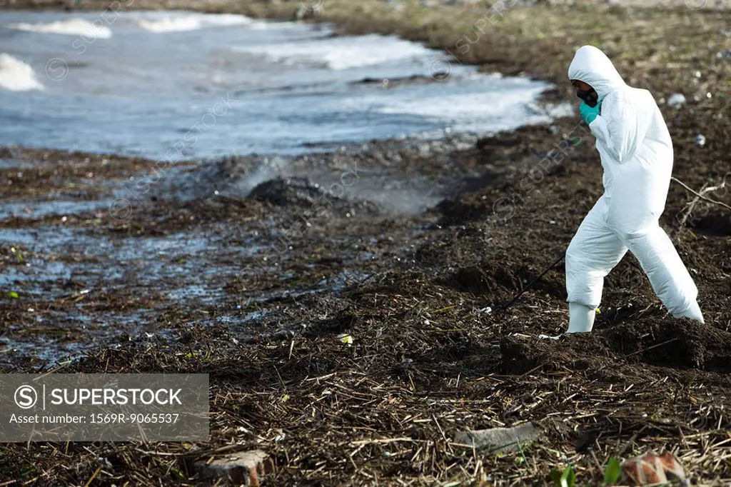 Person in protective suit walking along polluted shore