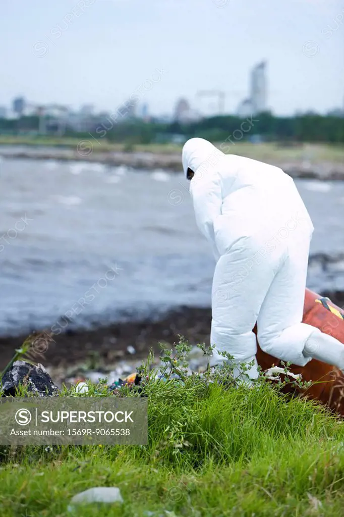 Person in protective suit cleaning up polluted shore
