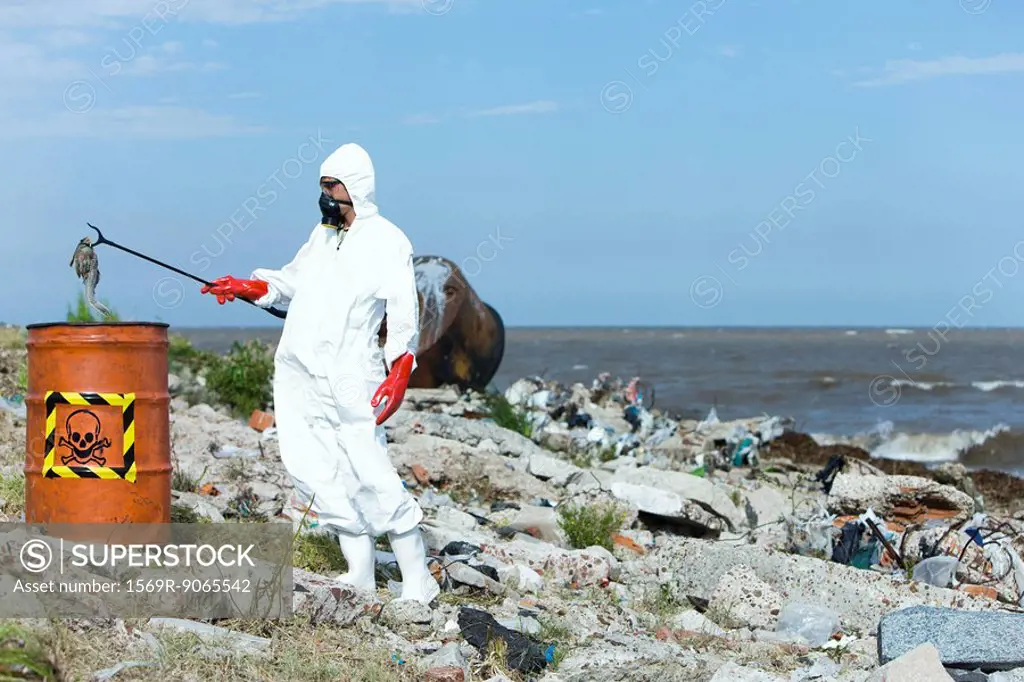 Person in protective suit placing dead fish in hazardous waste barrel