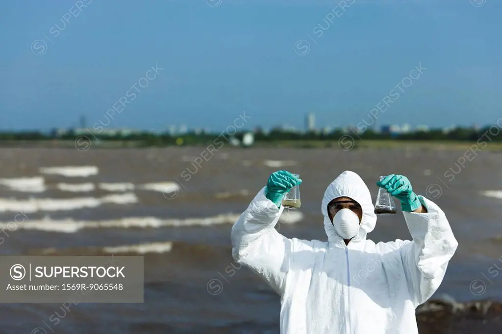 Person in protective suit holding up flasks filled with polluted water