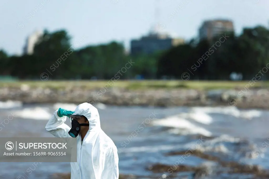 Person in protective suit looking at polluted water, side view