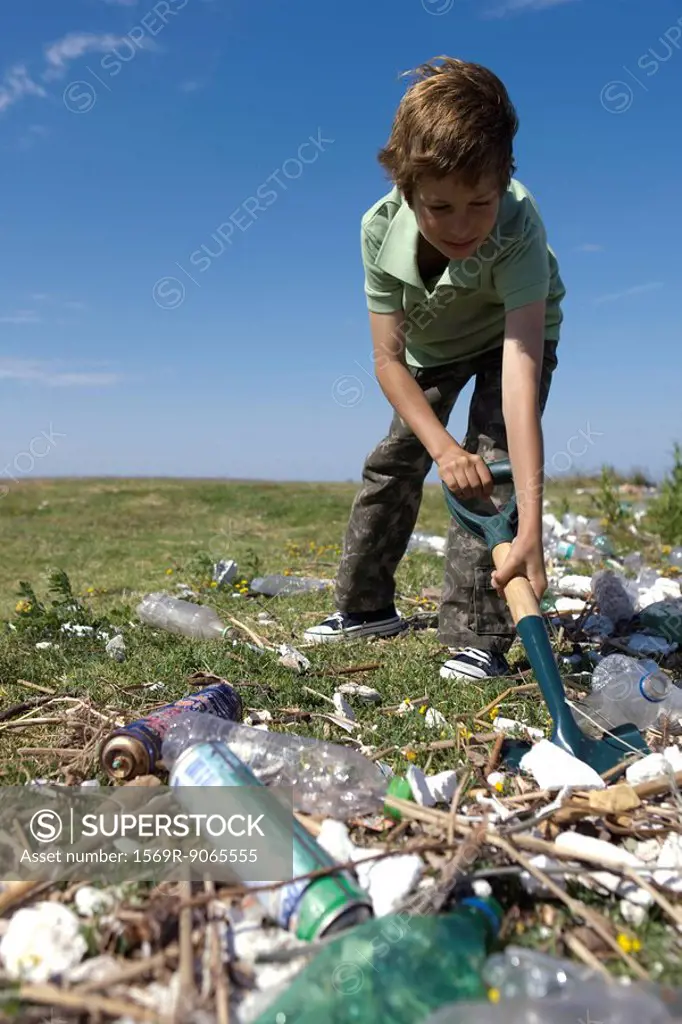 Boy shoveling trash in field