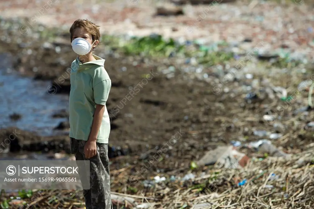 Boy standing on polluted shore, wearing pollution mask