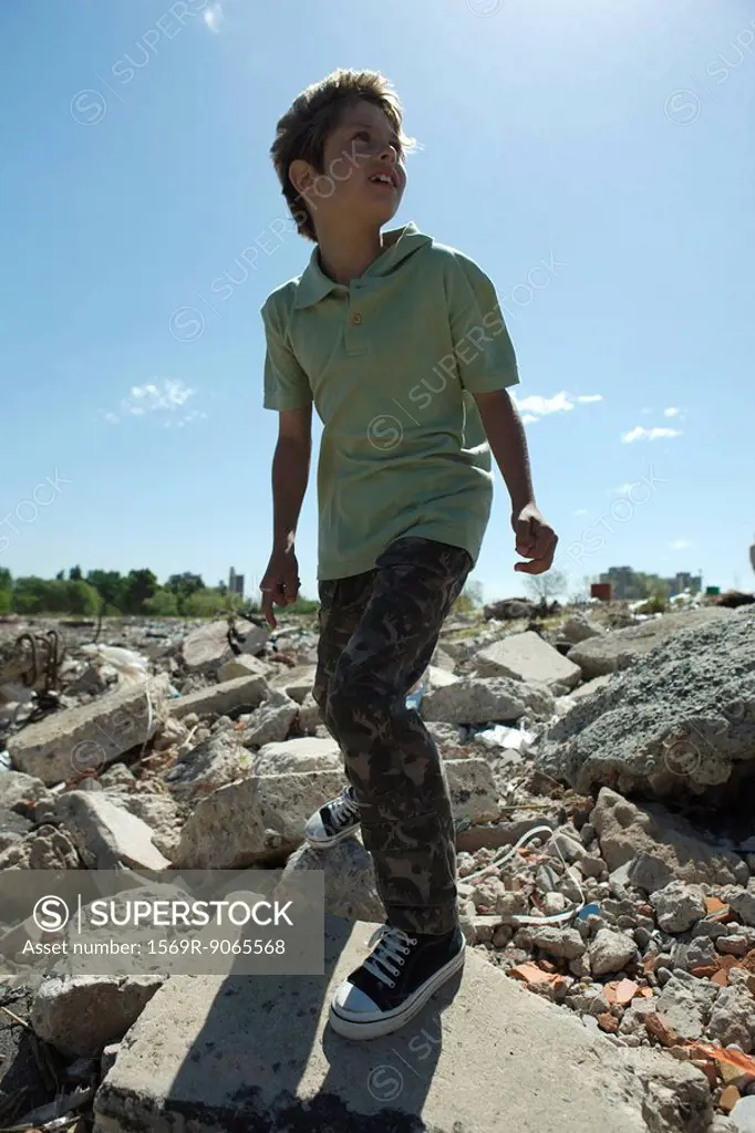 Boy standing on heap of rubble, backlit