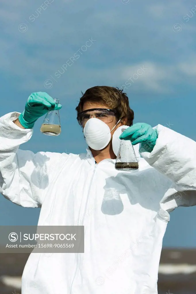 Person in protective suit holding flasks filled with polluted water