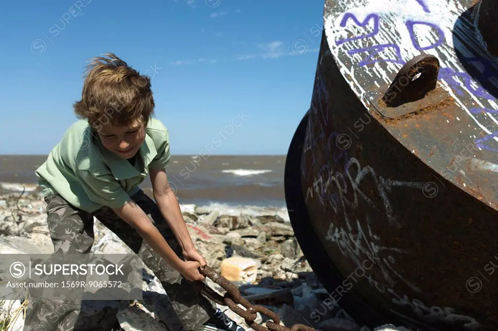 Boy pulling rusty chain on polluted shore