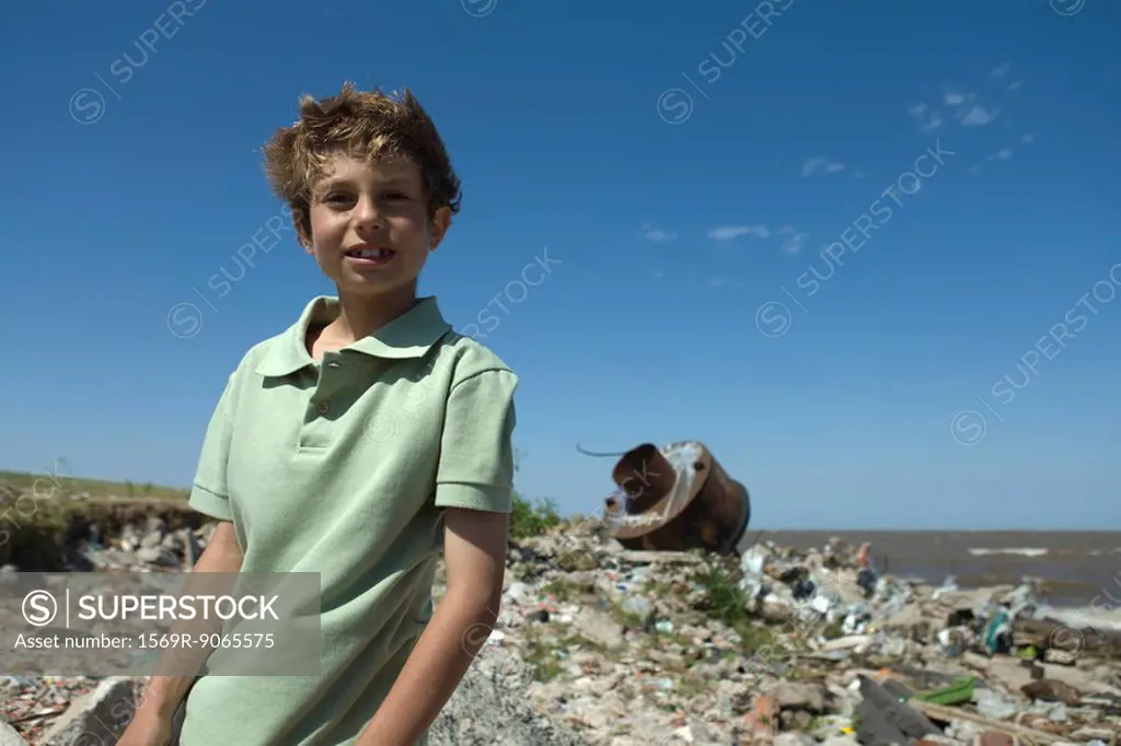 Boy standing on polluted shore, smiling at camera
