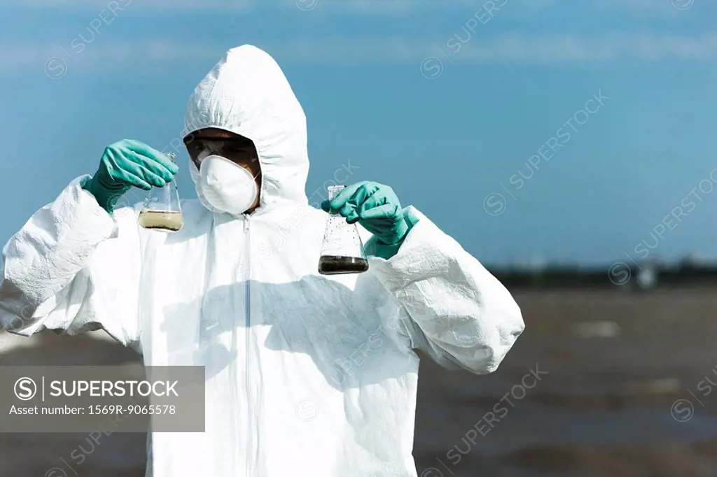 Person in protective suit holding flasks filled with polluted water