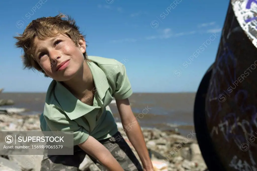 Boy on polluted shore, pulling large piece of scrap metal, close-up
