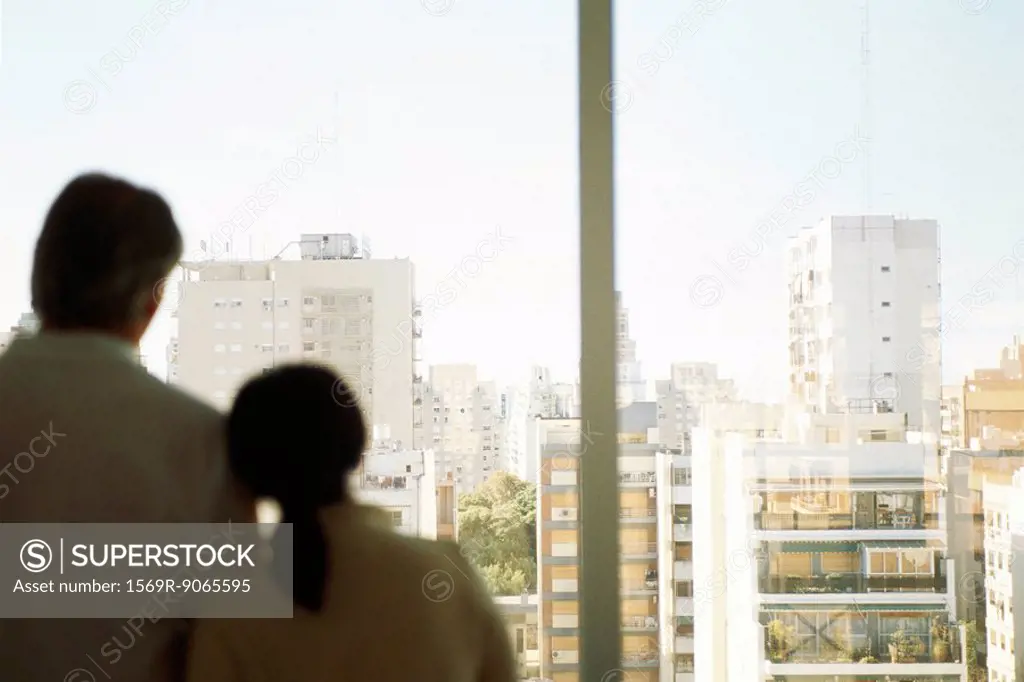 Couple, woman´s head on man´s shoulder, together at window looking at view of city