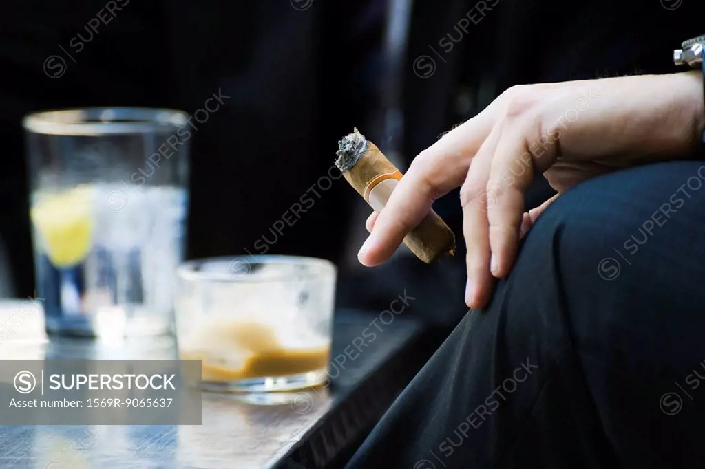 Man´s hand on knee holding smoking cigar, close-up