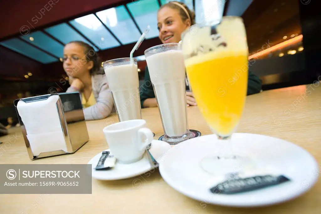 Teenage girls at cafe counter, milkshakes, glass of juice in foreground