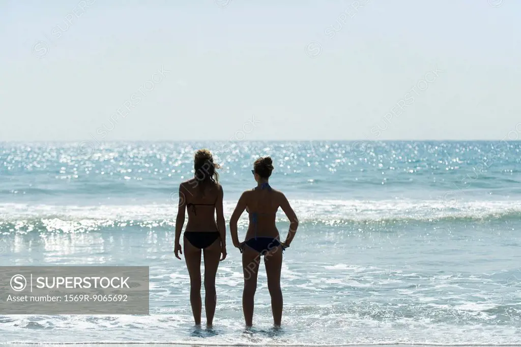 Teen girls standing side by side at the beach, looking at horizon