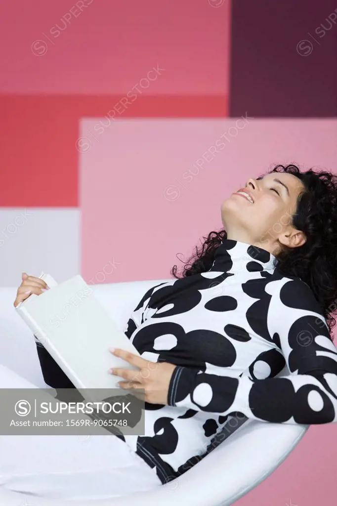 Woman enjoying book, leaning back with eyes closed, smiling