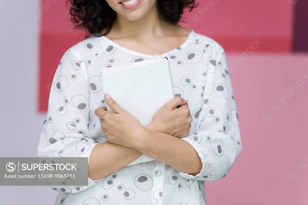 Woman holding book to chest, smiling, cropped