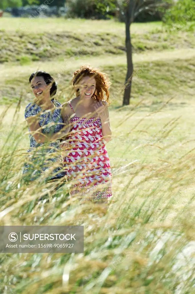 Two young women laughing together outdoors, tall grass in foreground