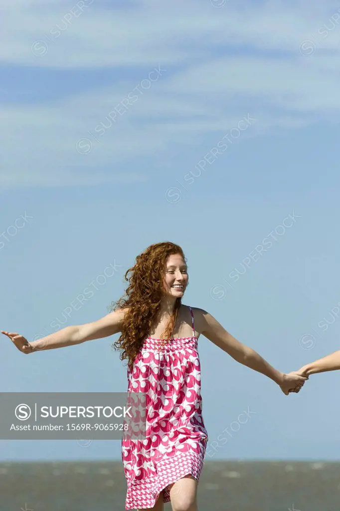 Young woman running with arms out, holding friend´s hand, cropped