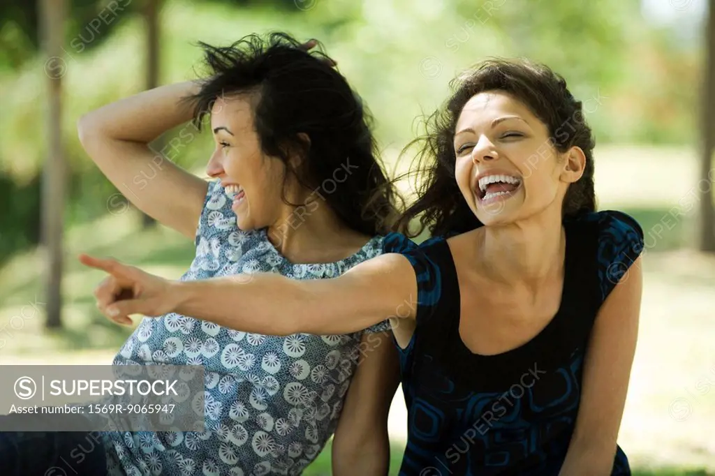 Two young women laughing outdoors, one pointing