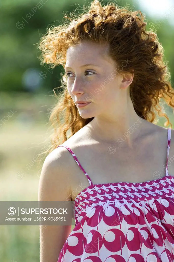 Young red haired woman outdoors, hair blowing in breeze, portrait