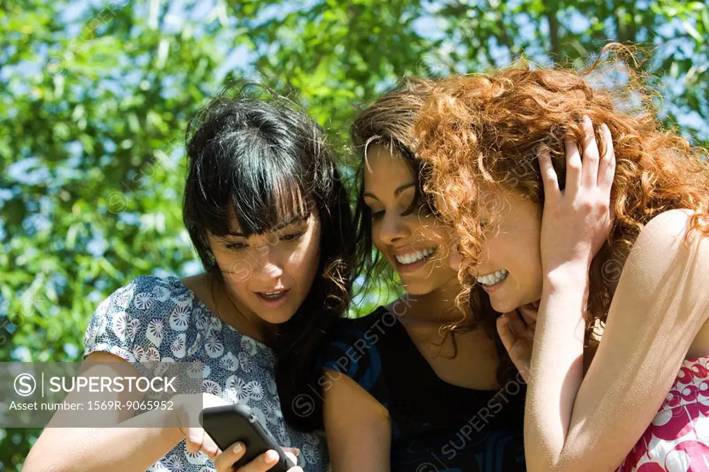 Three young women looking at cell phone outdoors