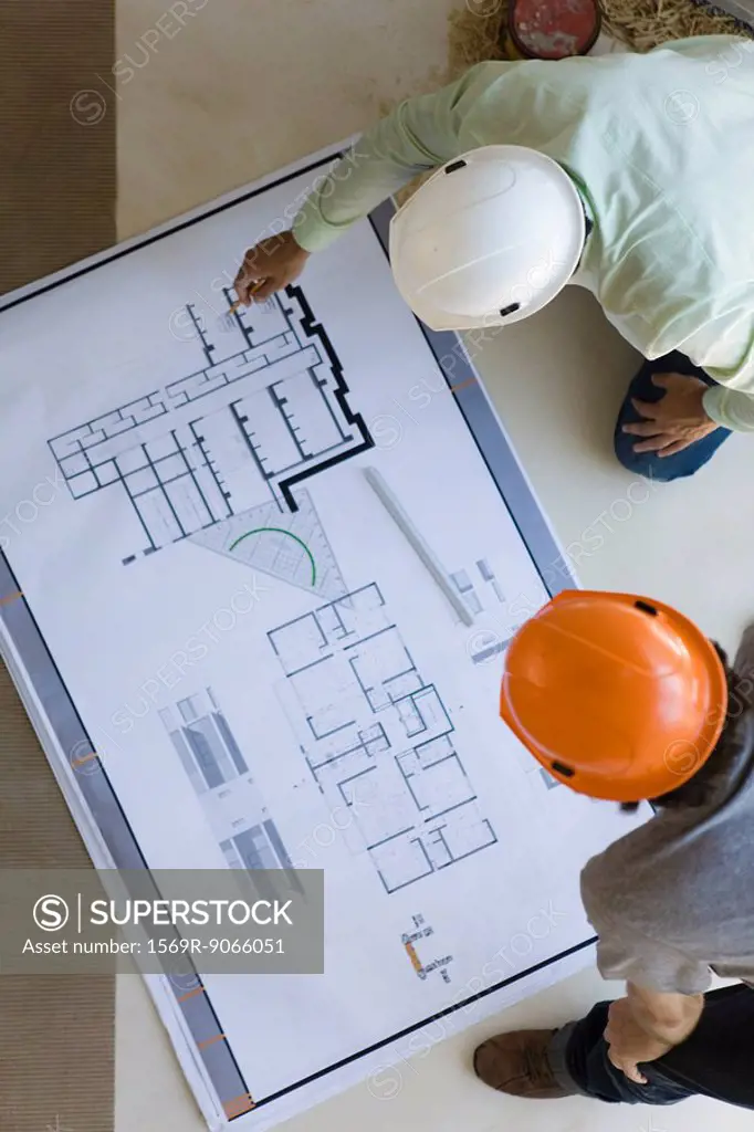 Two men crouching looking over blueprints spread out on floor