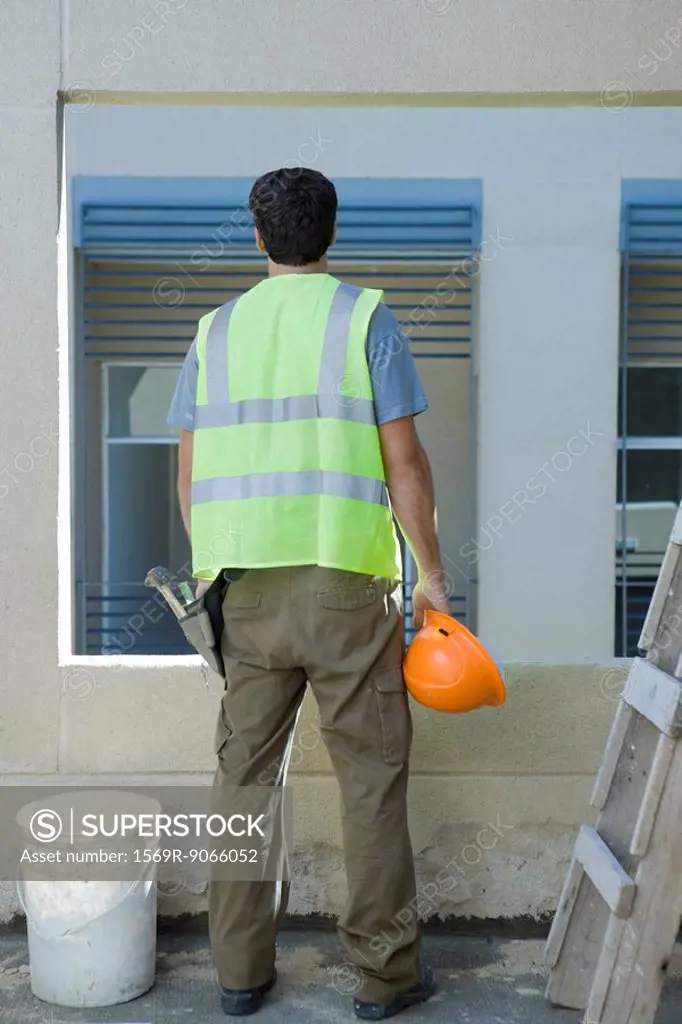 Construction worker holding hard hat looking out window