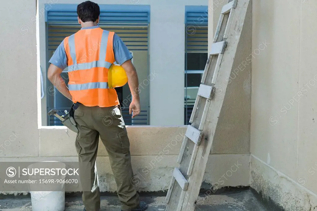 Construction worker with hand on hip looking out window, rear view