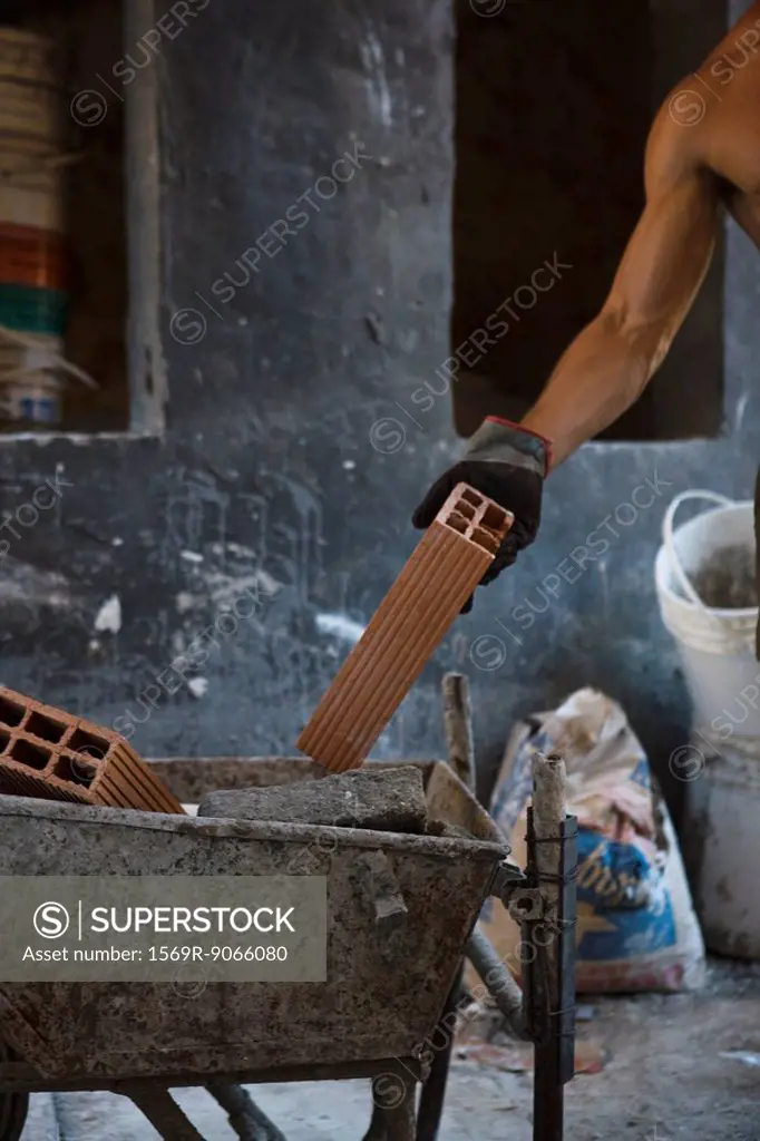 Construction worker placing brick in wheelbarrow