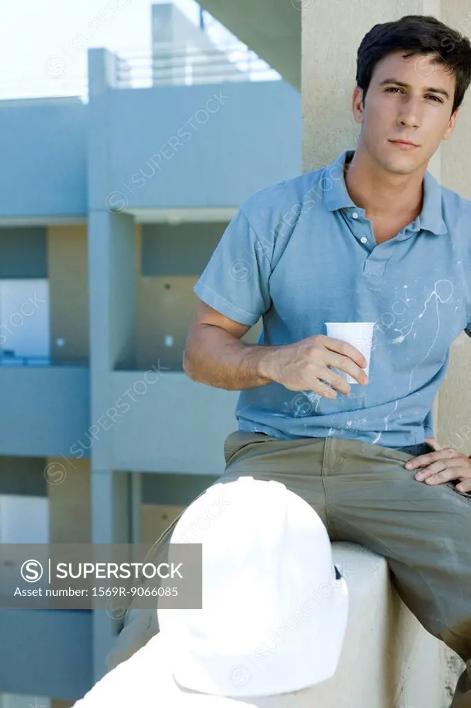 Construction worker sitting on ledge holding drink taking break