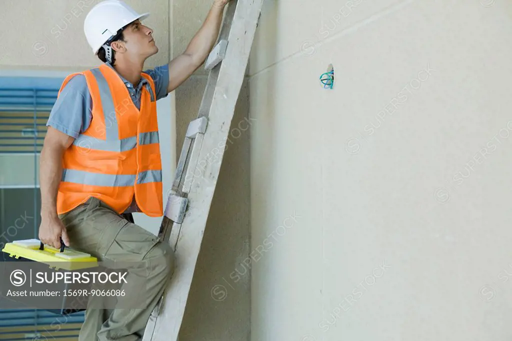 Man climbing ladder carrying toolbox