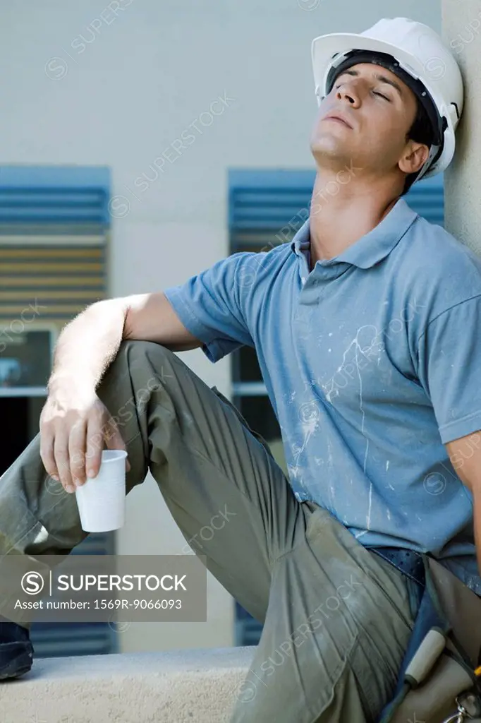 Construction worker sitting on ledge, leaning head back, eyes closed, taking break