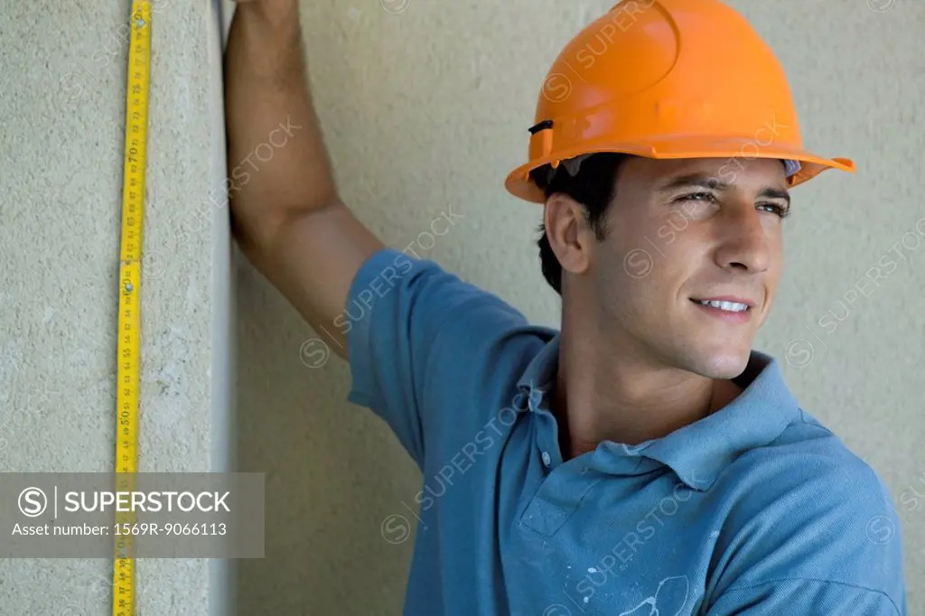 Construction worker holding ruler against wall, looking away
