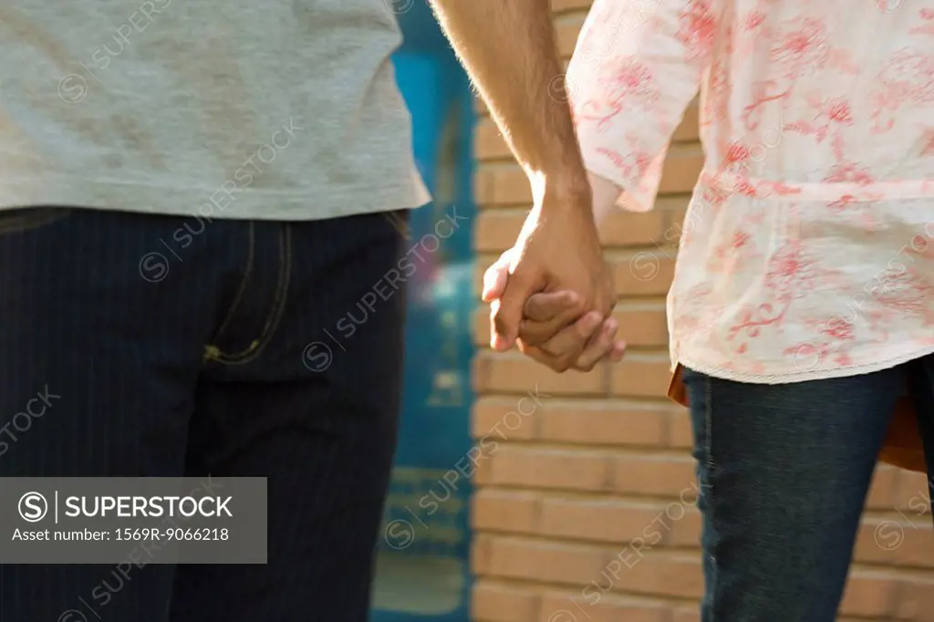 Young couple holding hands, walking, cropped view