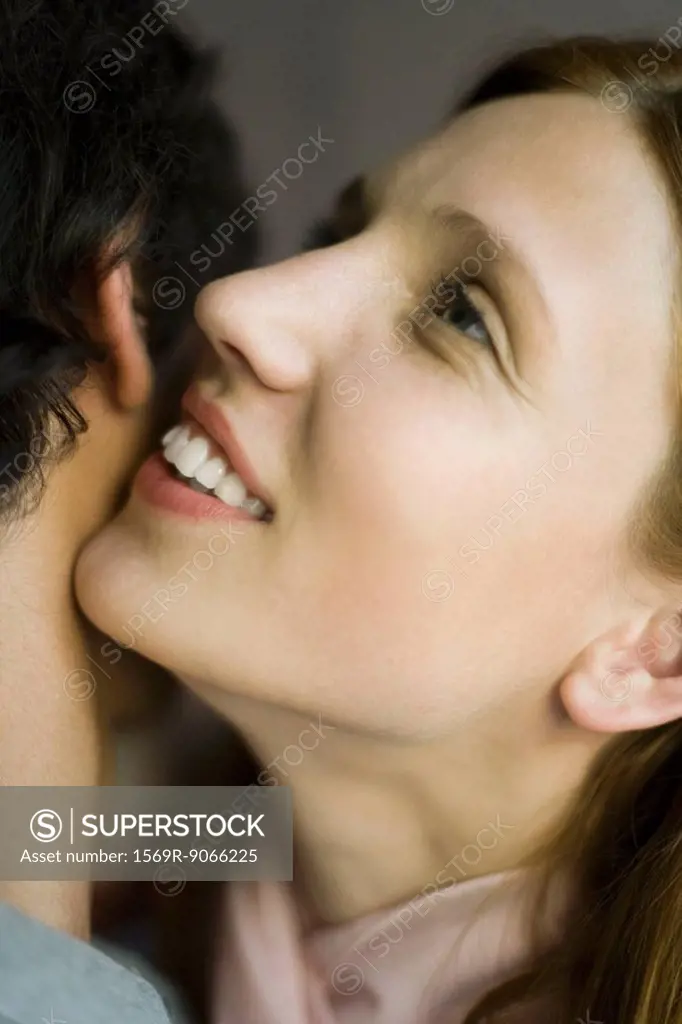 Young woman whispering in man´s ear, smiling, close_up