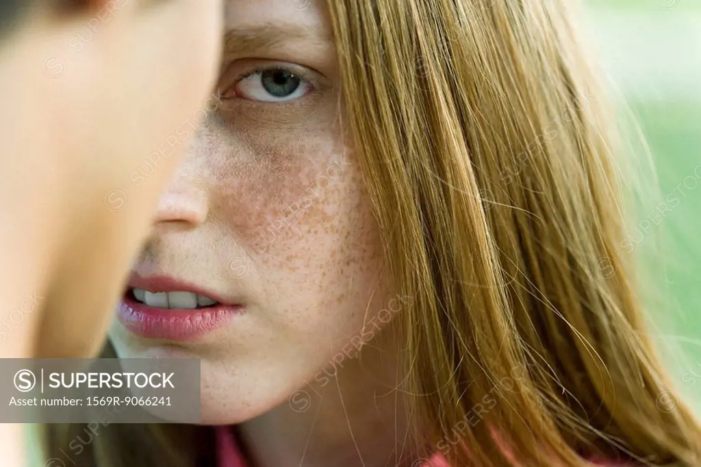 Young woman facing man, staring warily at camera, cropped