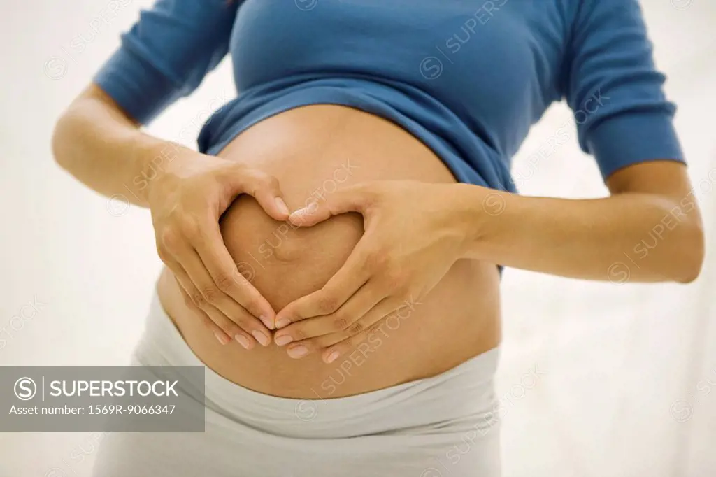 Pregnant woman holding hands in heart shape around navel