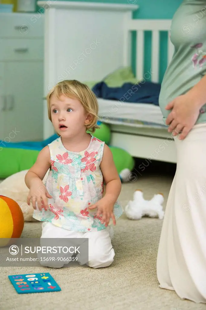 Little girl kneeling on floor in nursery beside pregnant mother, cropped