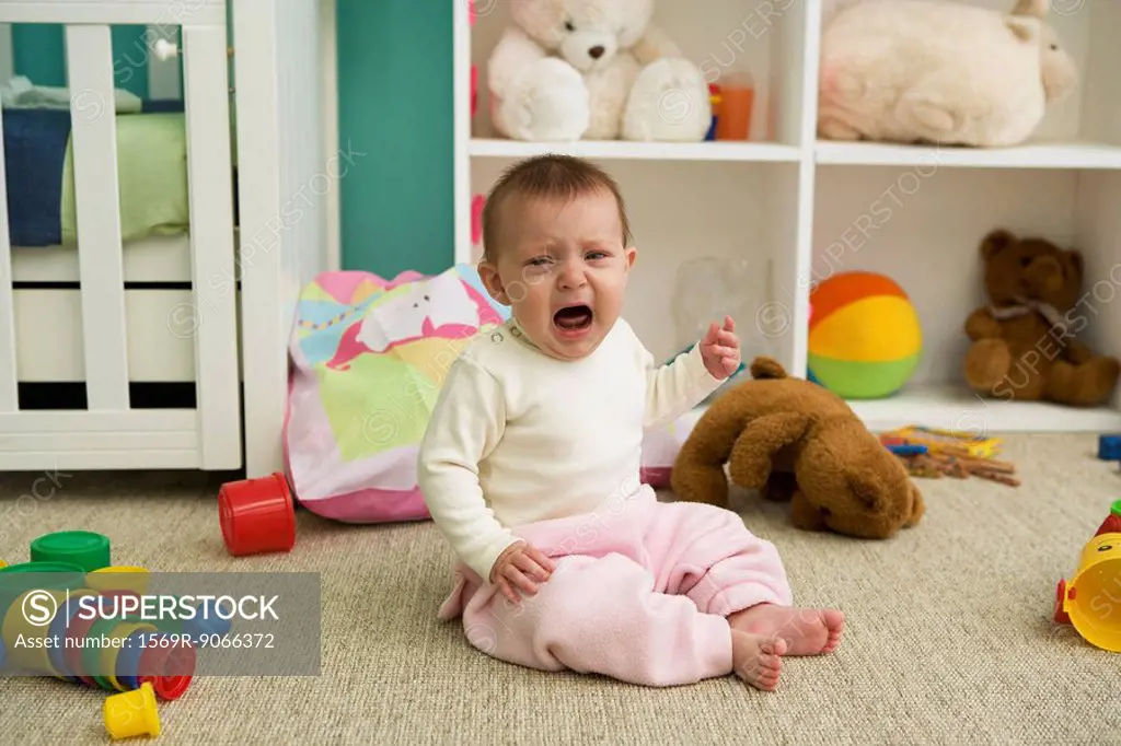 Baby sitting on floor of nursery, crying