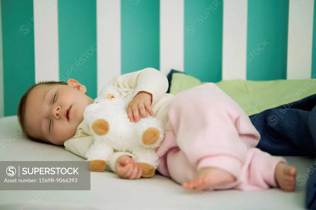Baby sleeping in crib, holding stuffed toy