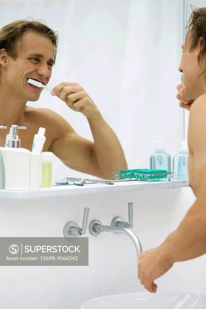 Man brushing teeth, looking at self in mirror