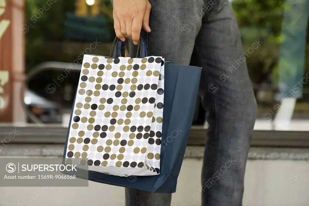 Man carrying shopping bags, shop window in background, cropped