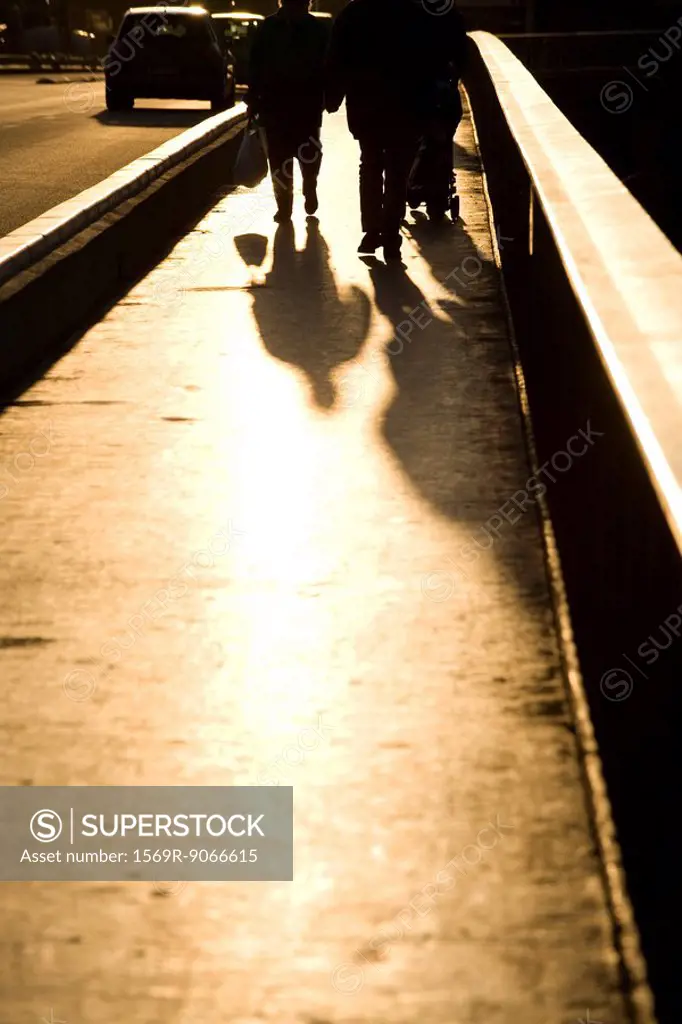 Pedestrians walking on sidewalk, backlit