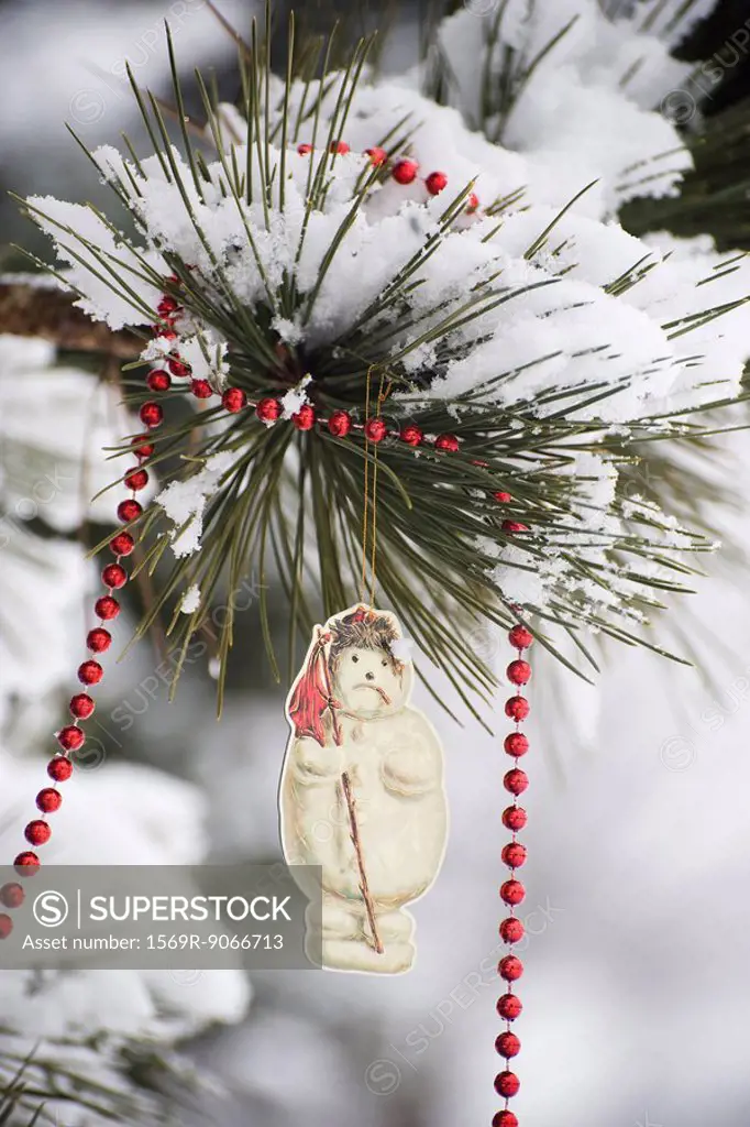 Snowman Christmas ornament and beaded garland hanging from snow_covered tree branch