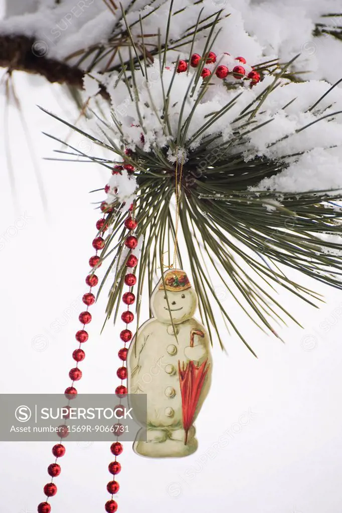 Snowman Christmas ornament and beaded garland hanging from snow_covered tree branch