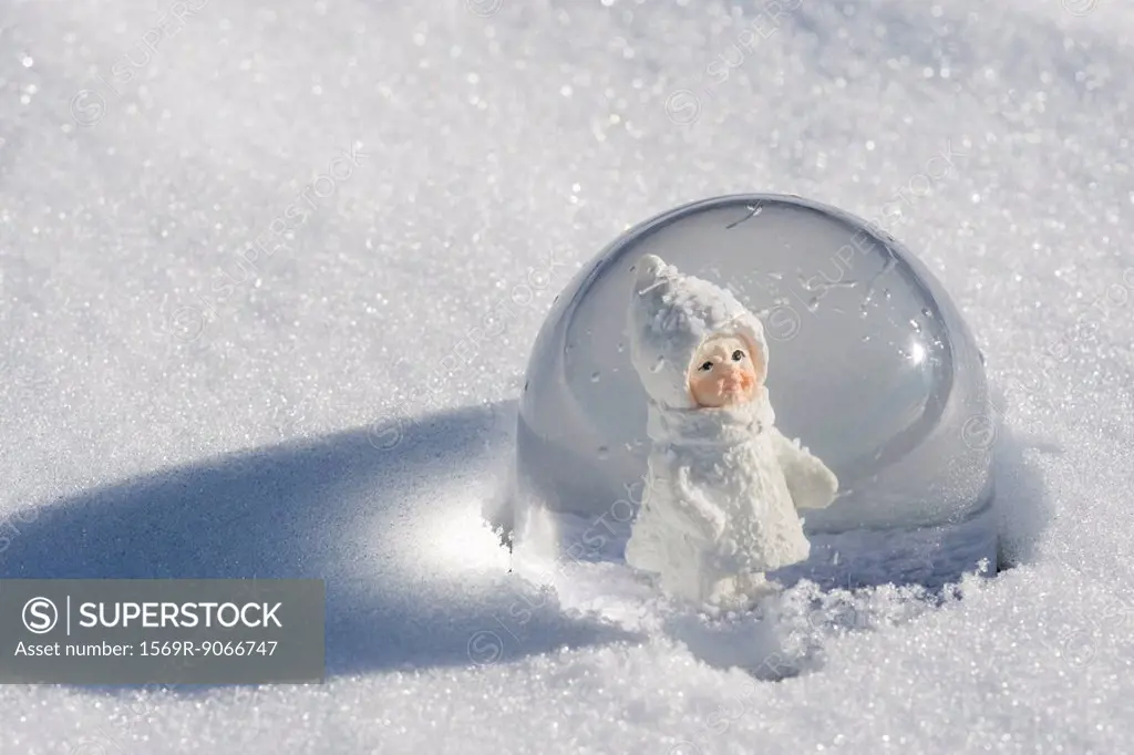 Snow globe in snow, figurine of little girl wearing winter coat and hat looking out