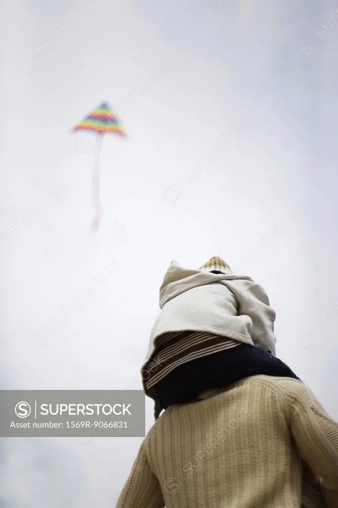 Father holding son on shoulders, kite flying in sky in background