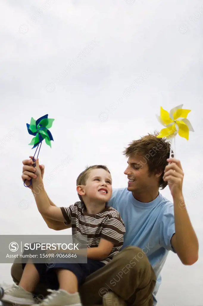 Little boy sitting on father´s lap, both holding pinwheels