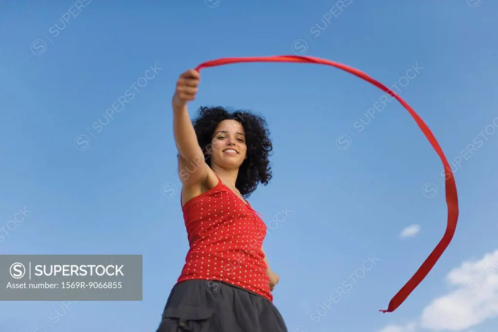 Young woman holding ribbon in wind, smiling, low angle view